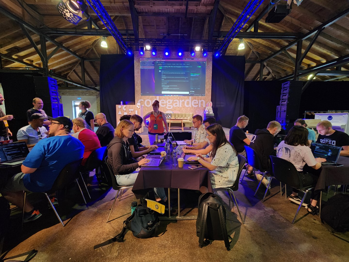 A group of people sitting at tables in front of the code garden stage participating in the hack-a-thon.